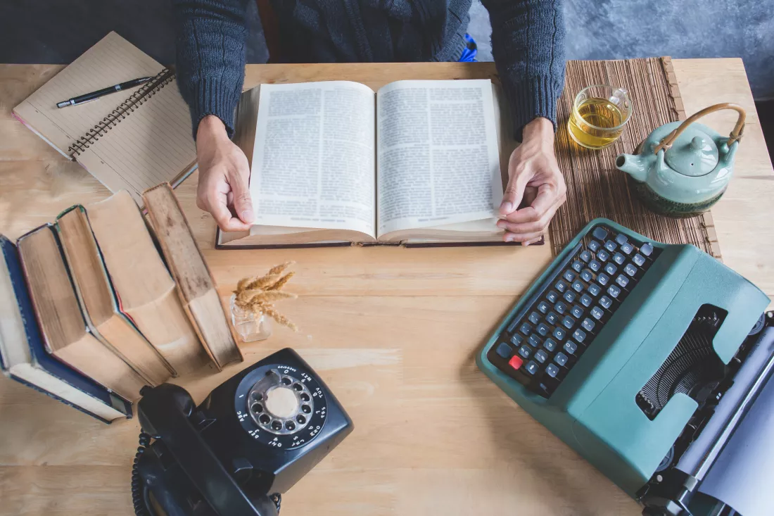 midsection-man-reading-book-with-old-objects-table