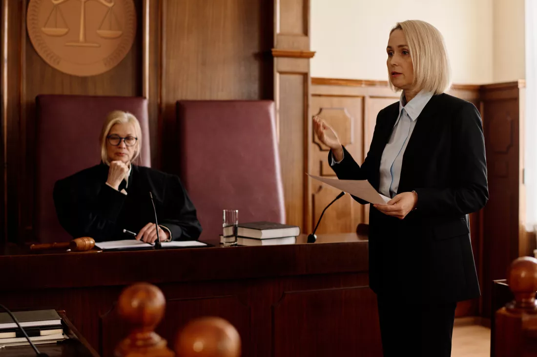 confident-blond-female-prosecutor-with-juridical-document-looking-suspect-his-attorney